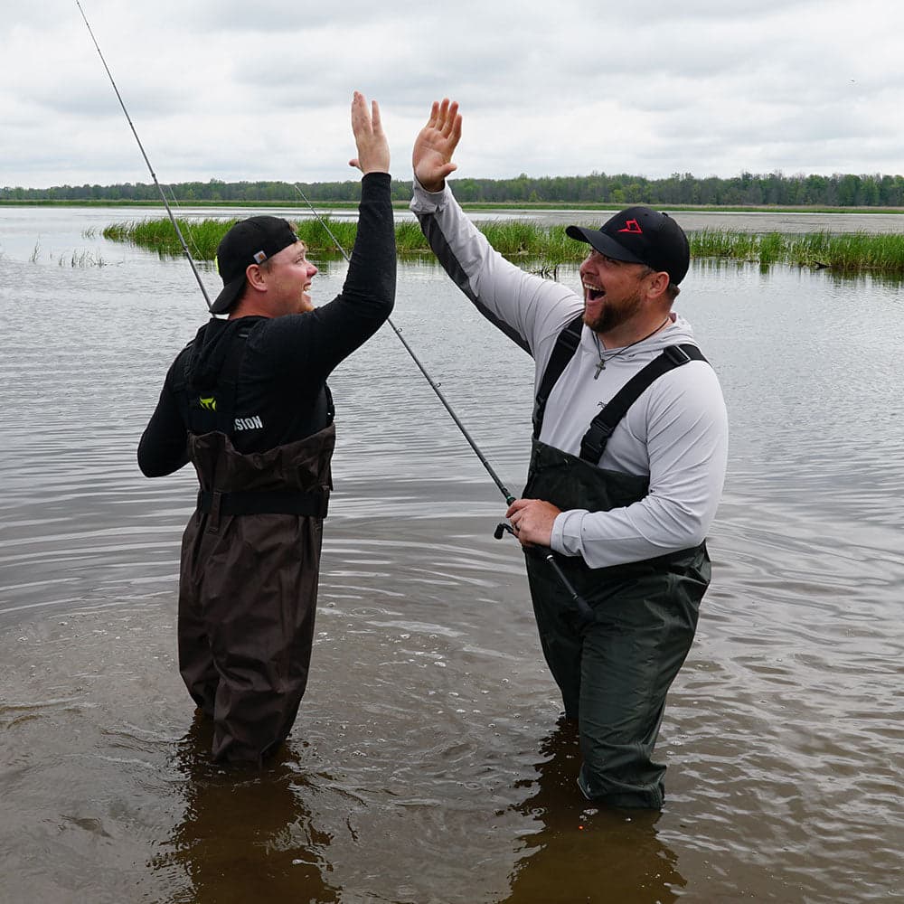 Two fisherman in waterproof waders high five in the river