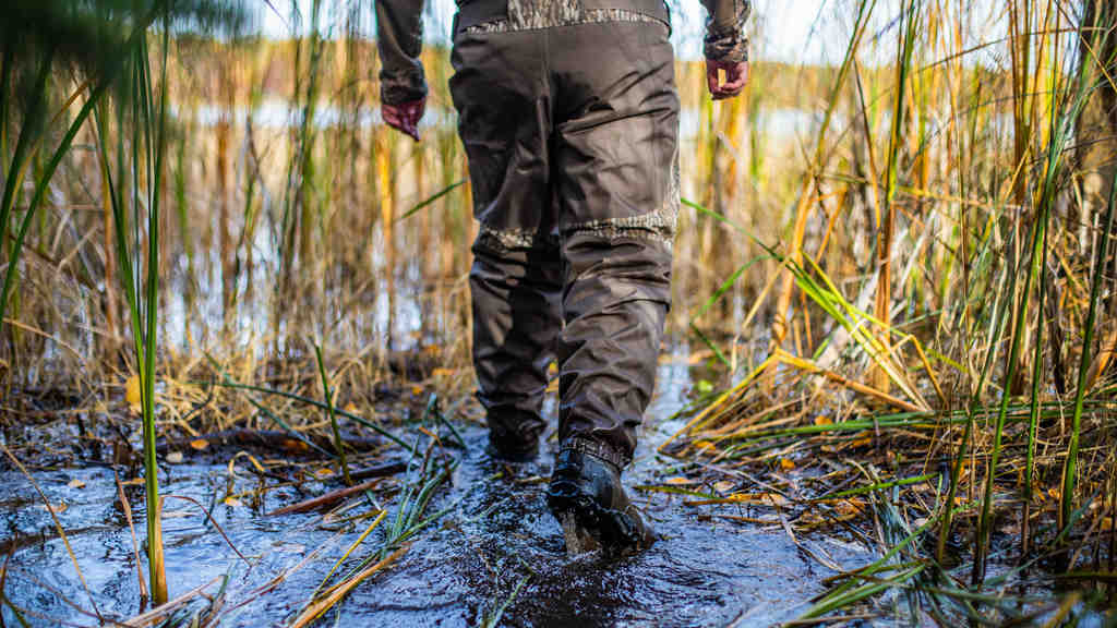 a man with breathable waders walks in the wet fields